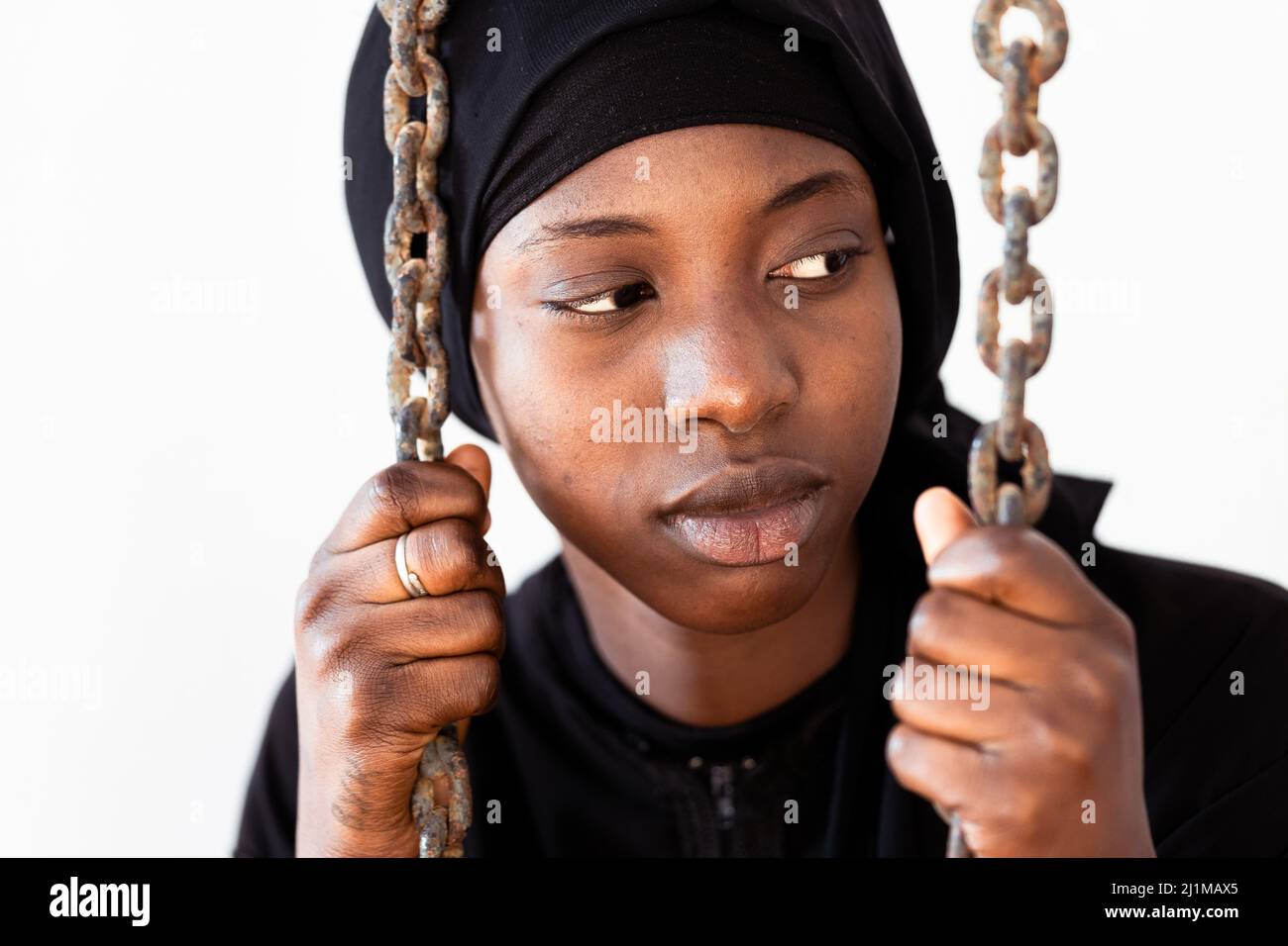 Sad young African girl behind the chains, symbolizing captivity, imprisonment or confinement; claim for justice and gender equality Stock Photo