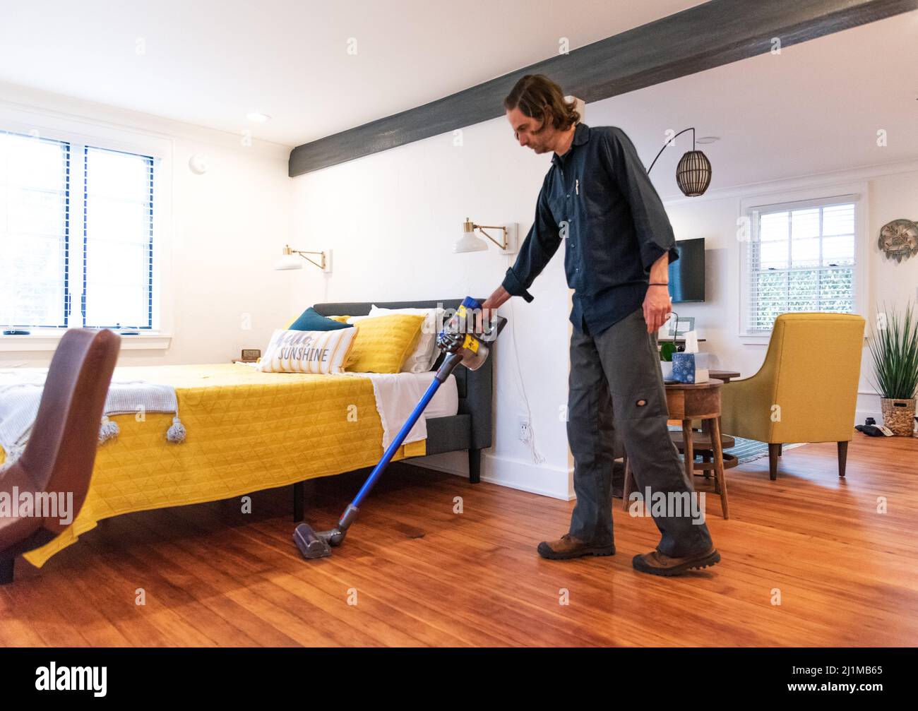 A man vacuums his airbnb rental studio to prepare for the next guest Stock Photo