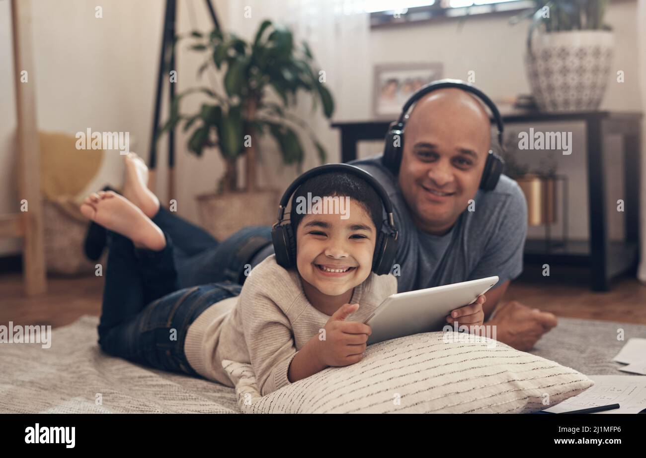 It doesnt feel like schoolwork when its so much fun. Shot of an adorable little boy using a digital tablet and headphones with his father at home. Stock Photo