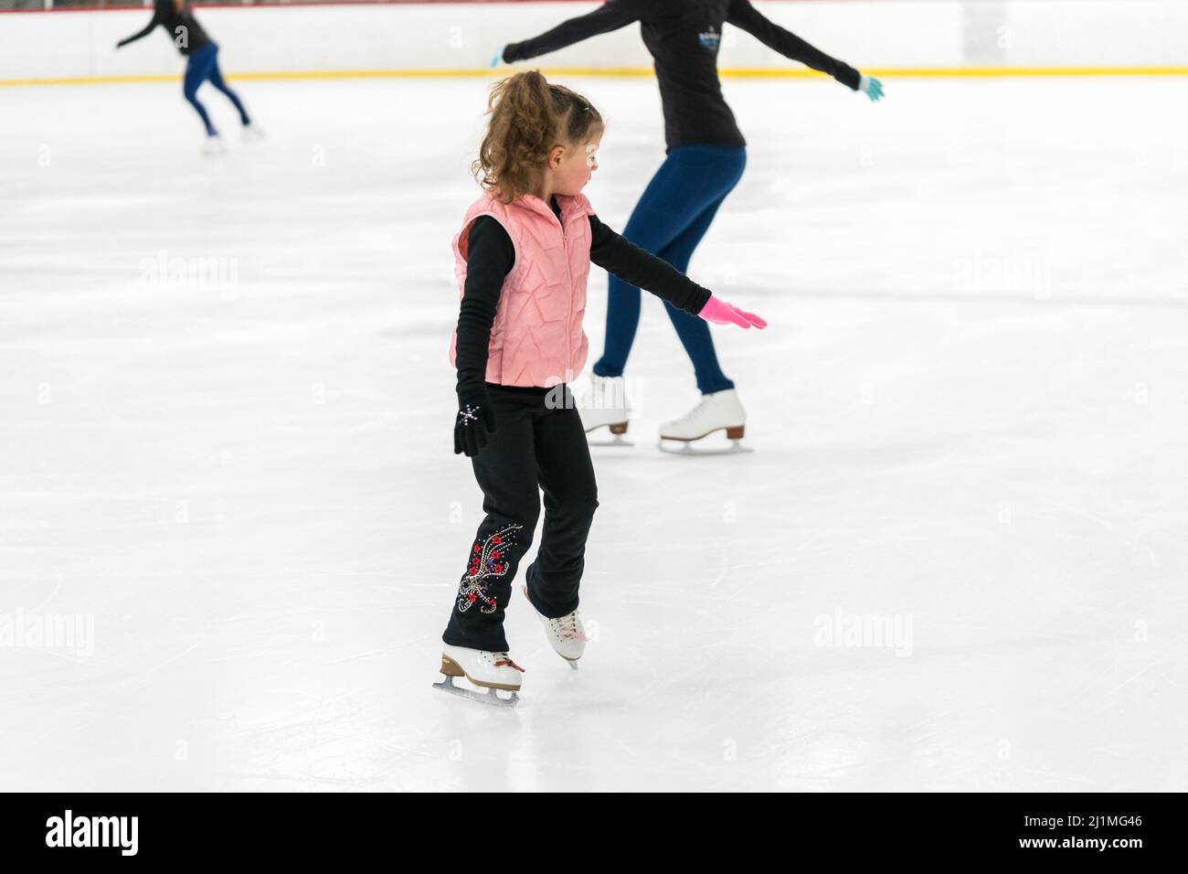 Little girl practicing figure skating elements on indoor ice skating