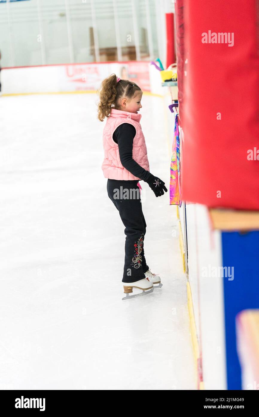 Little girl practicing figure skating elements on indoor ice skating