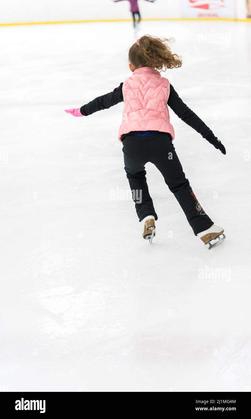 Little girl practicing figure skating elements on indoor ice skating