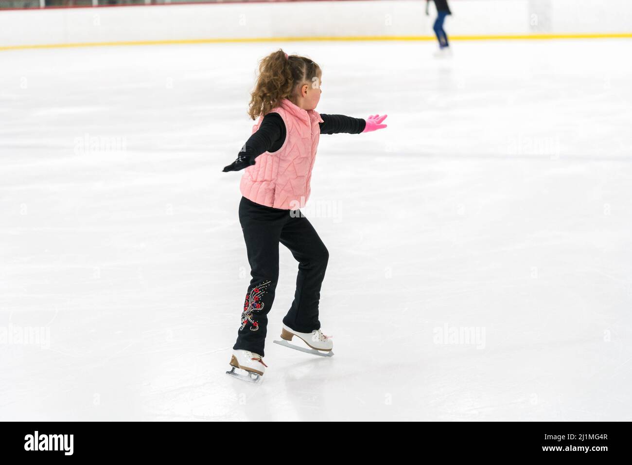 Little girl practicing figure skating elements on indoor ice skating