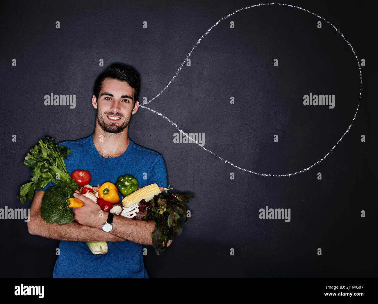 Eat clean and feel good. Studio portrait of a young man carrying vegetables next to an illustration of a thought bubble against a dark background. Stock Photo