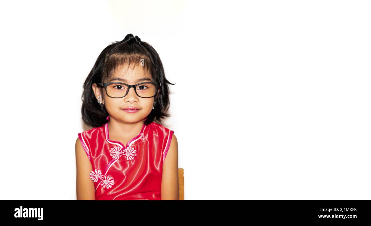 picture of beautiful liitle girl in red chinese dress wearing eye glasses sitting on chair Stock Photo