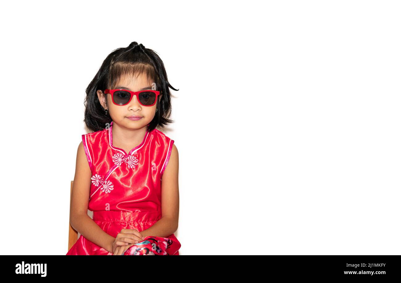 picture of beautiful liitle girl in red chinese dress wearing sun glasses sitting on chair Stock Photo