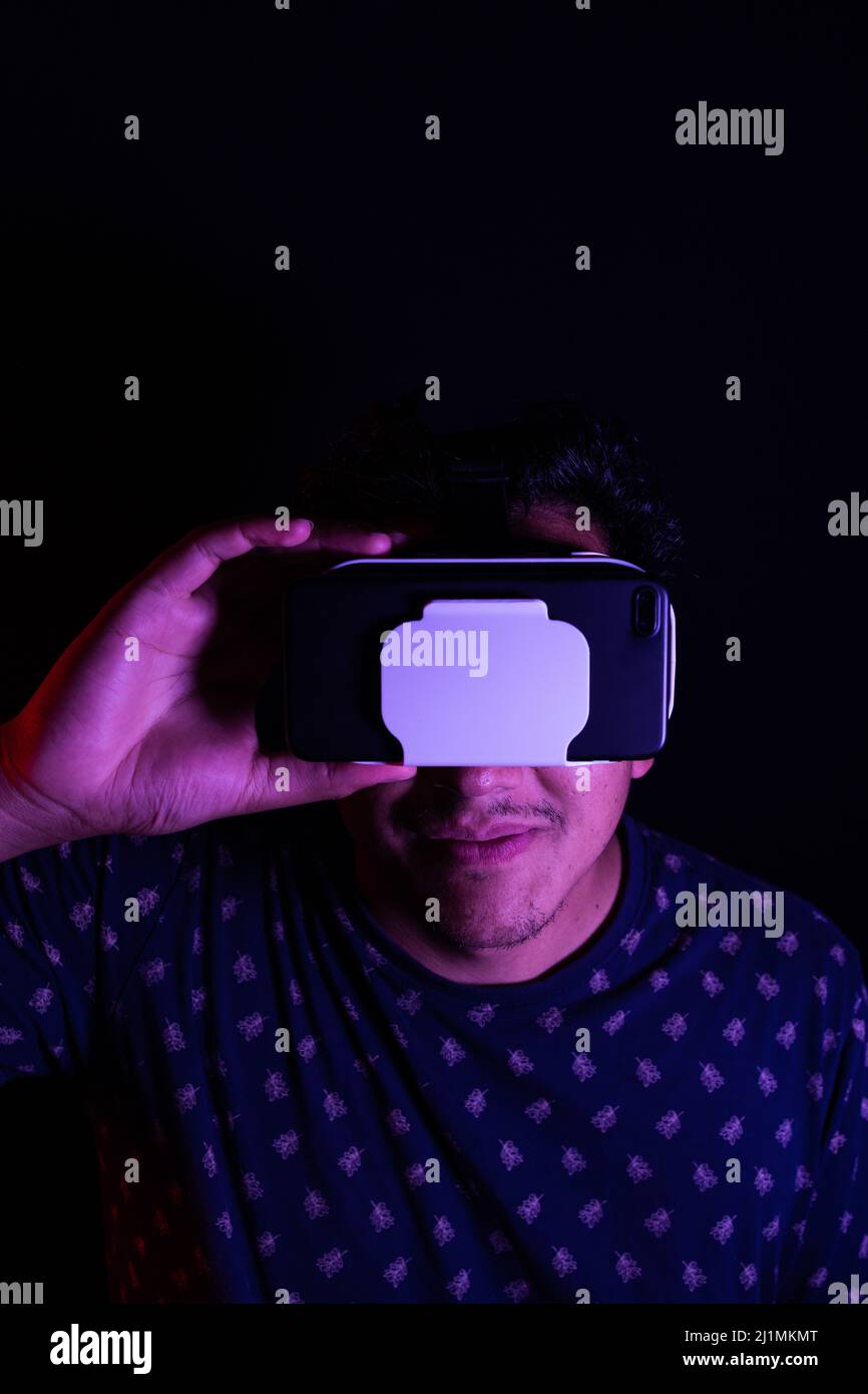 Young latin man using Virtual Reality VR Headset 3D Glasses. Dark backdrop. Low key. Copy space Stock Photo
