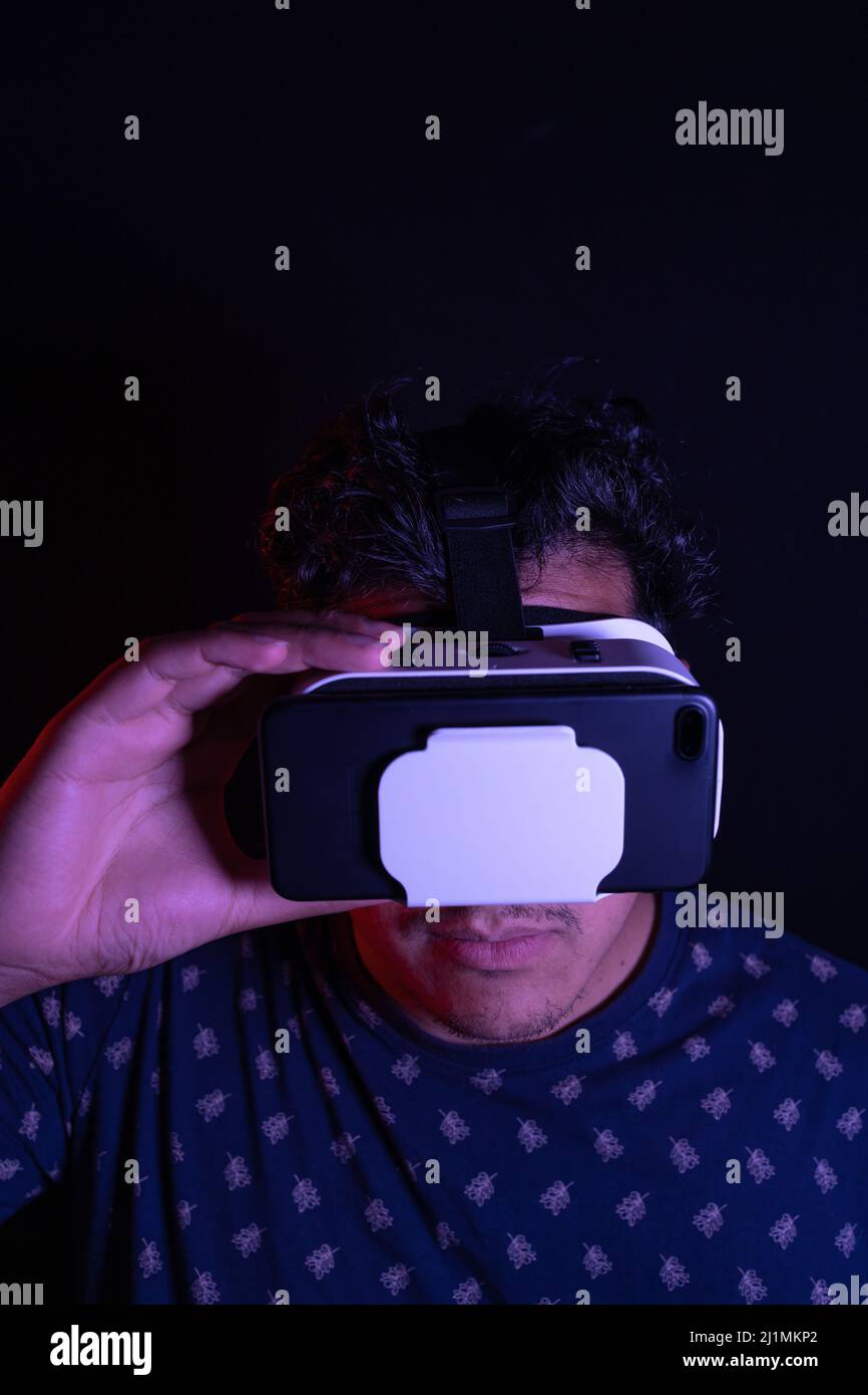 Young latin man using Virtual Reality VR Headset 3D Glasses. Dark backdrop. Low key. Copy space Stock Photo