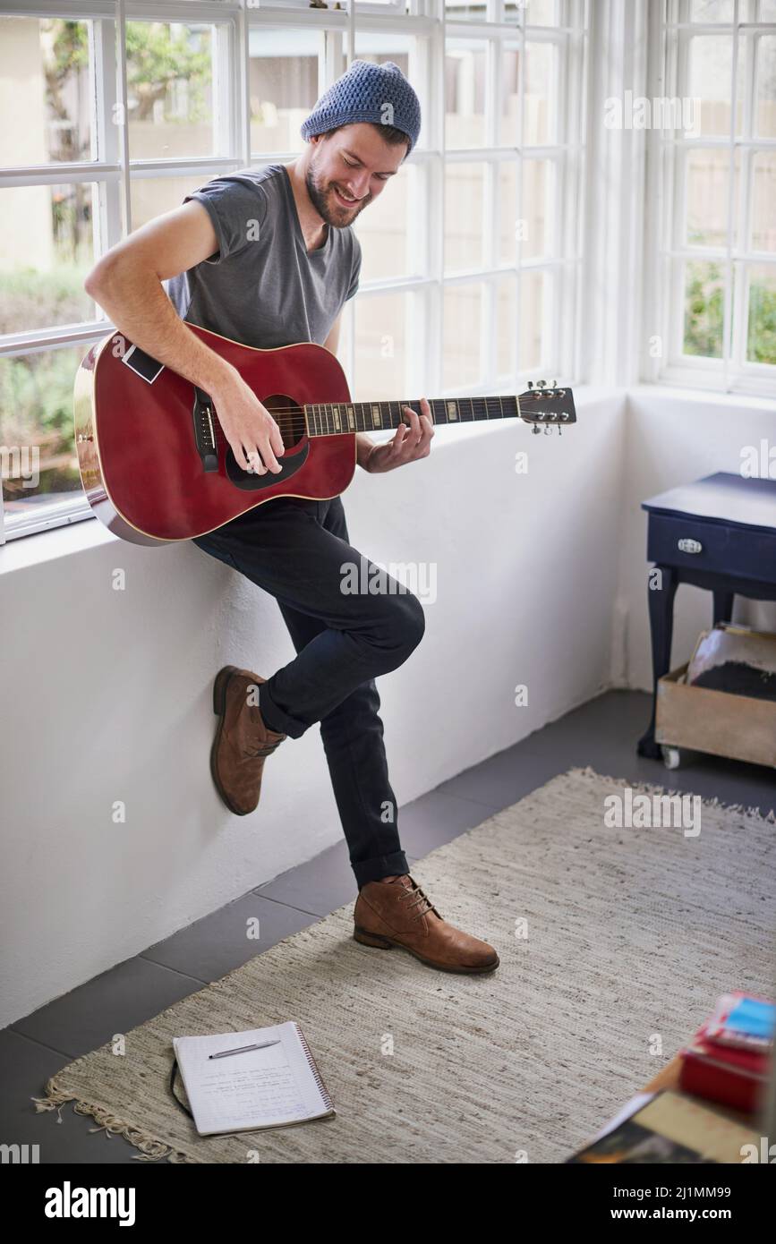 Practising for his upcoming gig. Shot of a handsome young man playing a guitar at home. Stock Photo