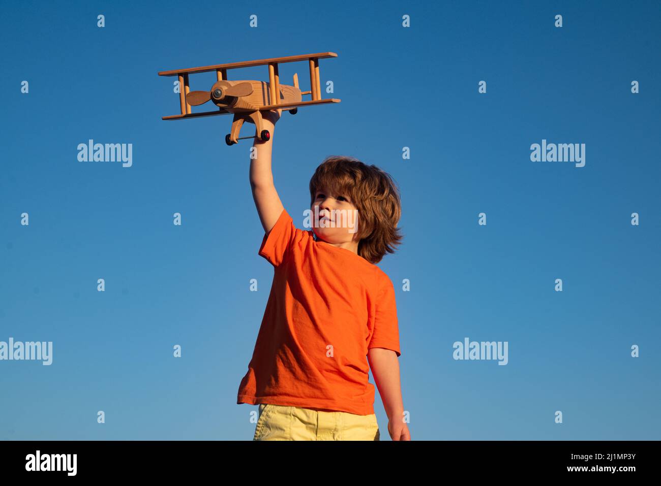 Child boy 7 year old playing with wooden toy airplane, dream of becoming a pilot. Childrens dreams. Child pilot aviator with wooden plane. Stock Photo