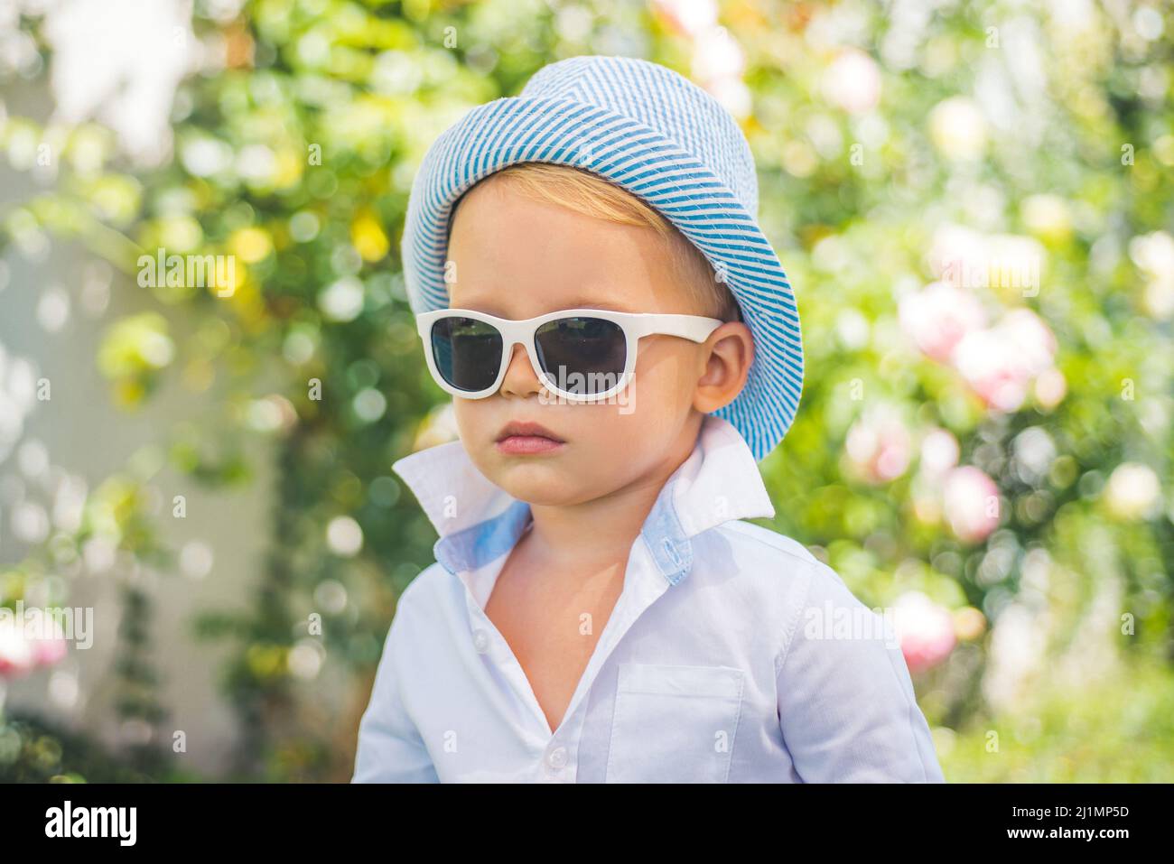 Kids fashion. Happy child in sunglasses and hat, adorable lovely kid. Joyful portrait of small child on green nature background outside. Stock Photo
