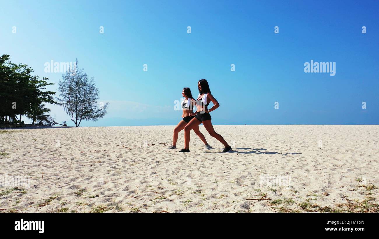 A Two Caucasian pretty females in gym outfit exercising on the sandy ...
