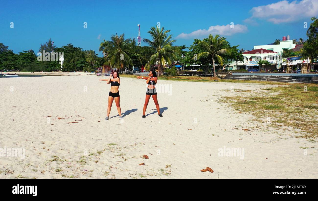 A Two Caucasian pretty females in gym outfit exercising on the sandy ...