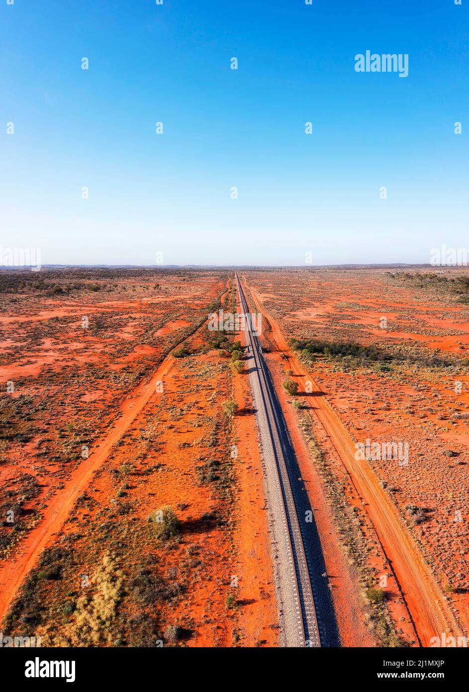 Endless single railway line in red soil outback of Australia near Broken hill mining city - aerial vertical panorama. Stock Photo