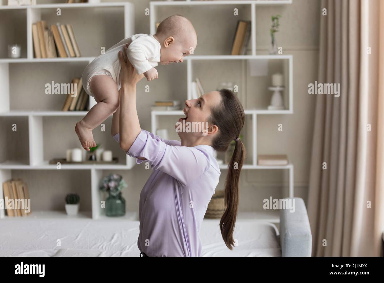 Smiling young mother lifting in air laughing adorable newborn baby. Stock Photo