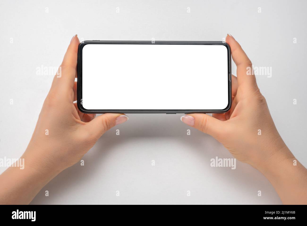 phone mockup. female hands hold phone horizontally. cell phone in horizontal position with blank white screen on gray table background. woman using he Stock Photo