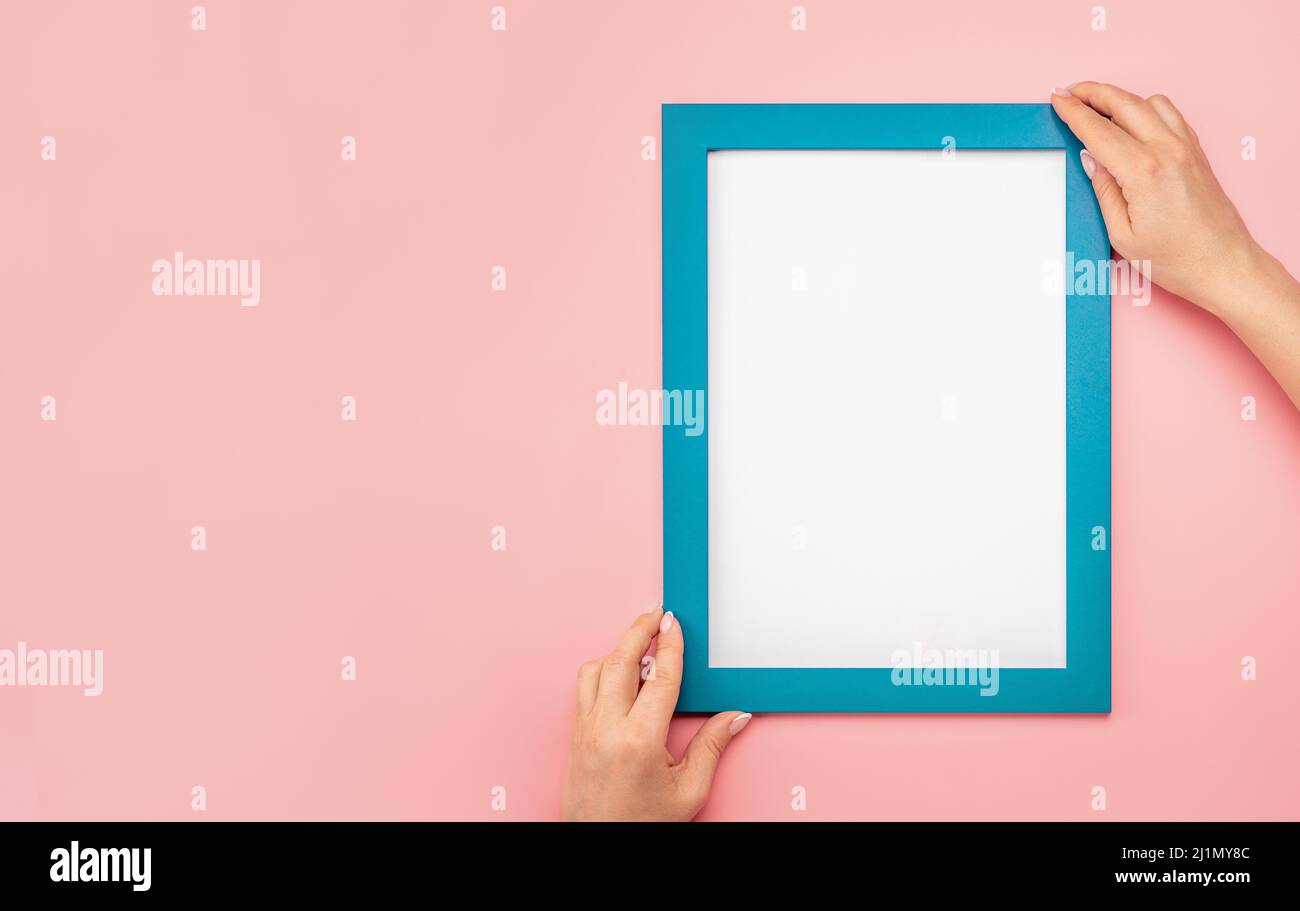Woman hold blank diploma frame on pink wall background. Hanging photo frame mockup on pink wall. Picture frame mockup. Holding frame. Female hands hol Stock Photo