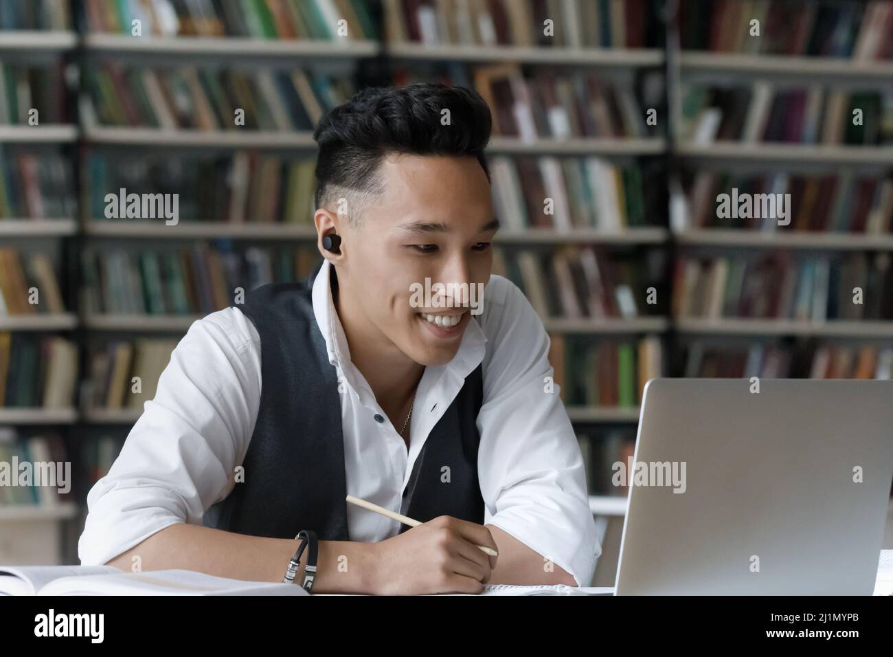 Smiling Korean guy sit in library studying online using laptop Stock Photo