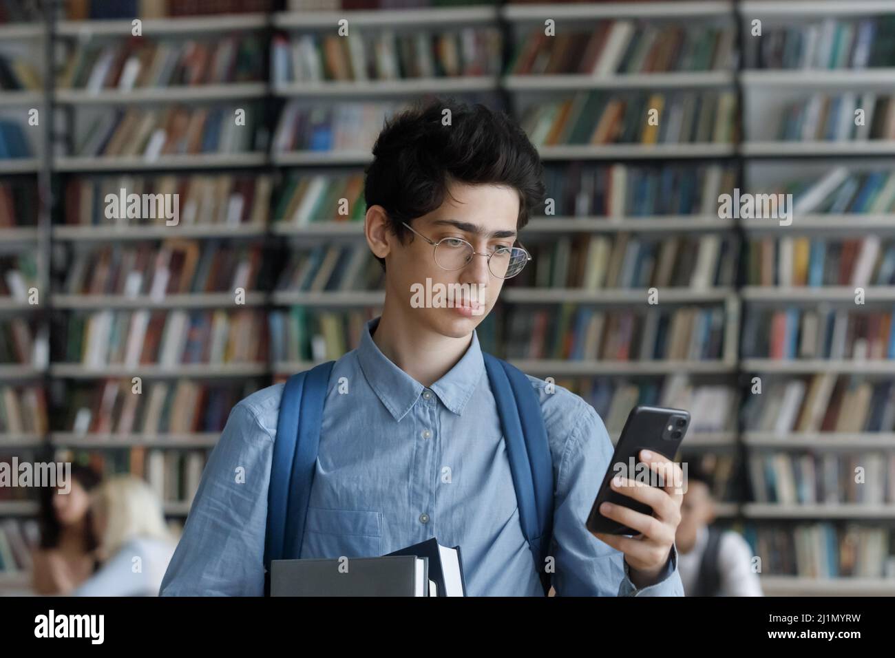Student guy standing in library holds cellphone check messages Stock Photo