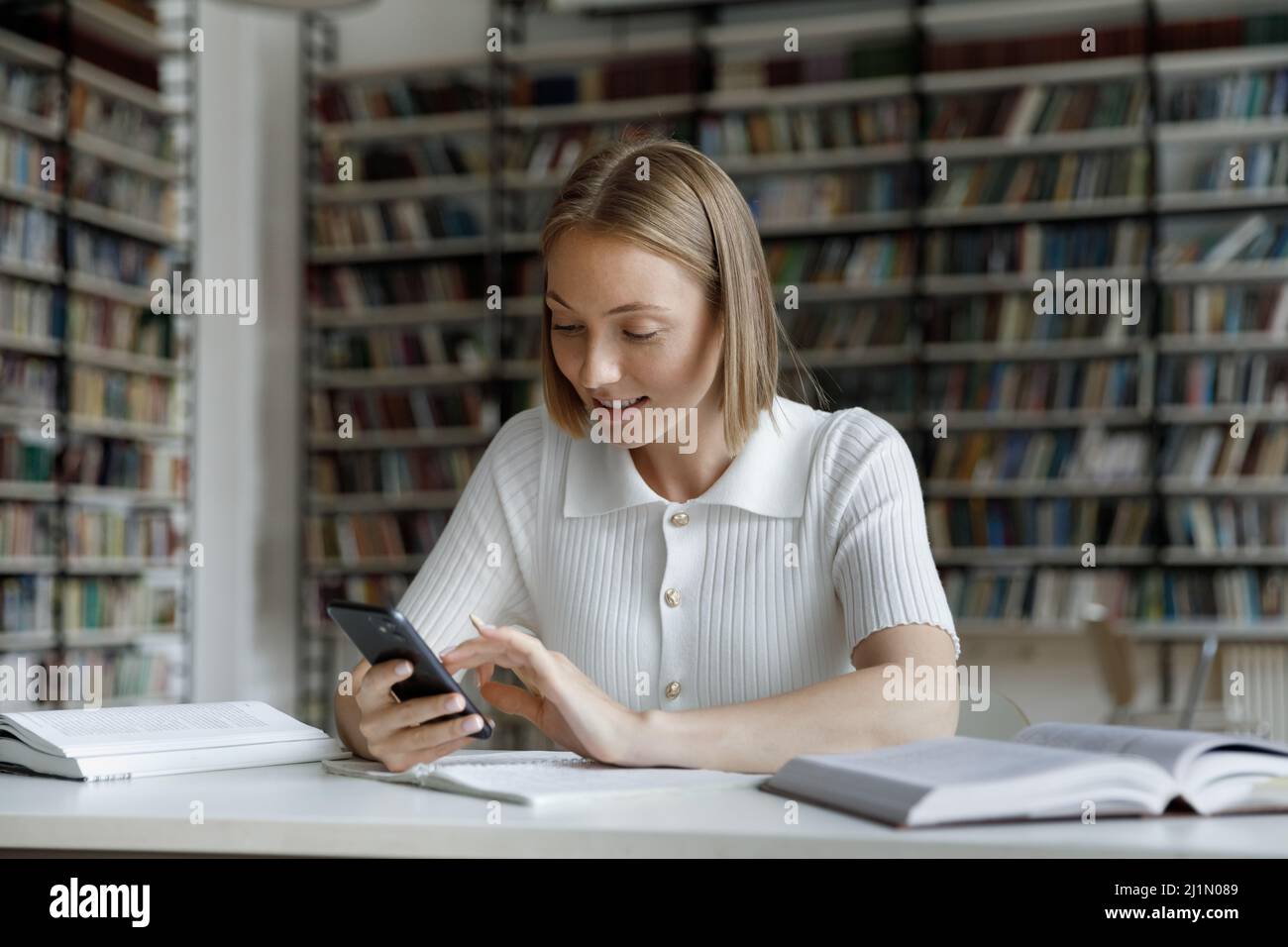 Student girl sit at desk in library use smartphone Stock Photo