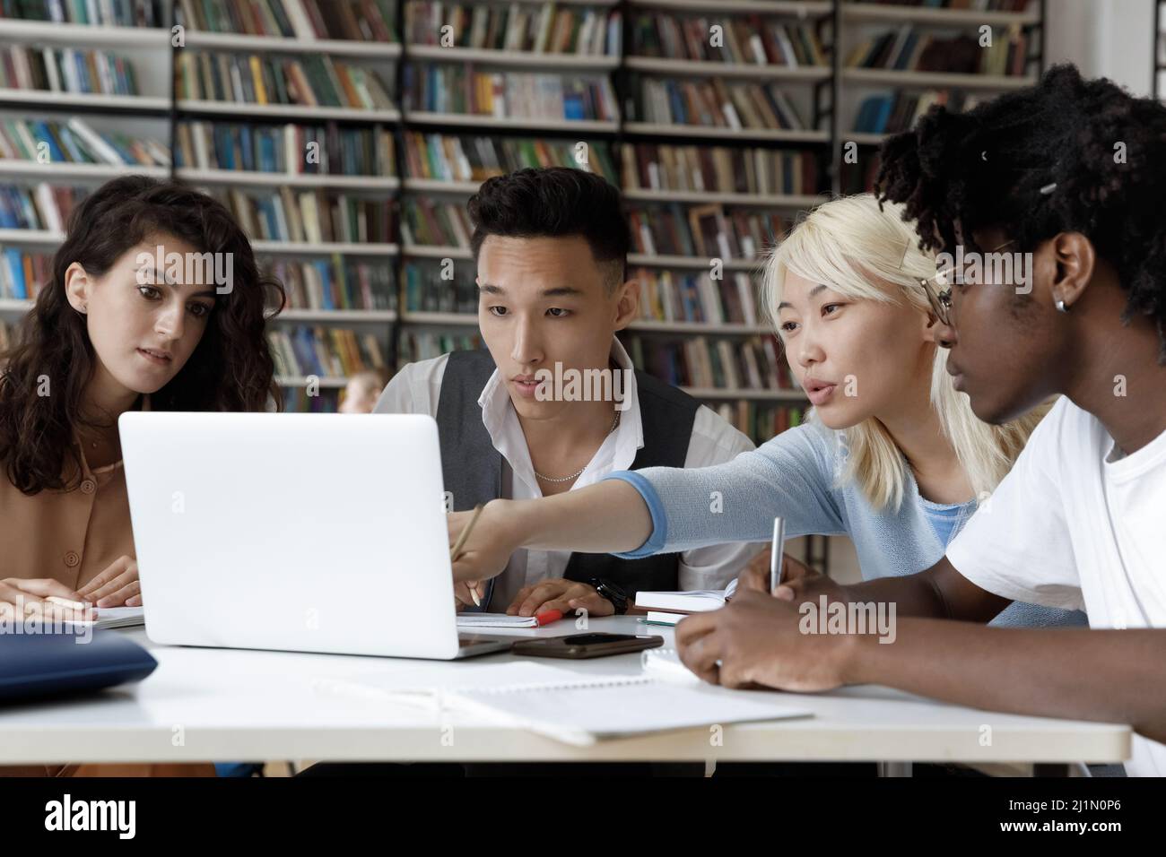 Four multi ethnic student studying in library using laptop Stock Photo