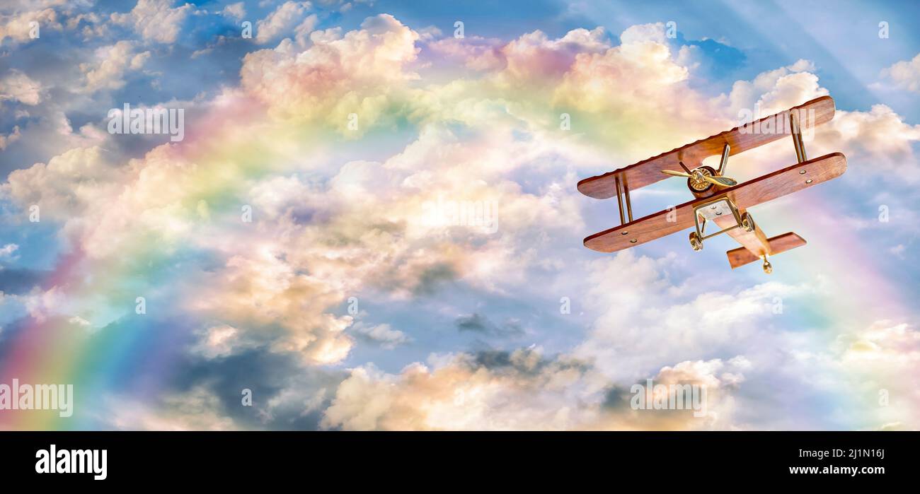Toy plane is flying on a sunny day with a rainbow and clouds in the sky with copy space. Stock Photo