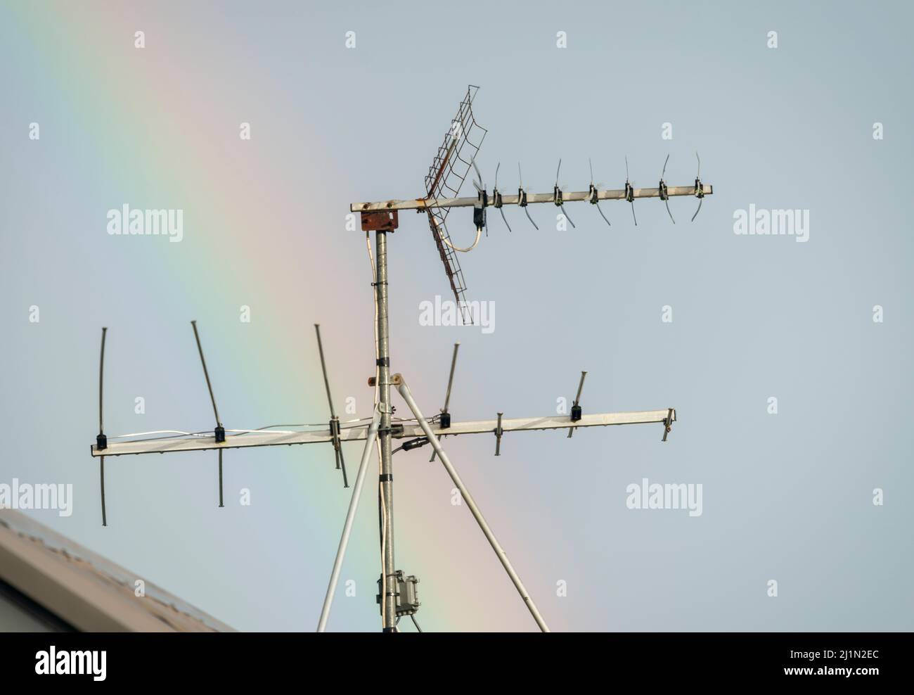 TV antenna on the rooftop of a house, against a rainbow across the sky. Stock Photo