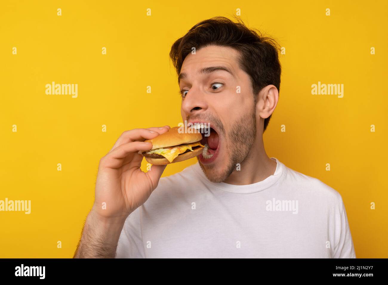 Funny Guy Holding Burger Biting Sandwich At Studio Stock Photo. 