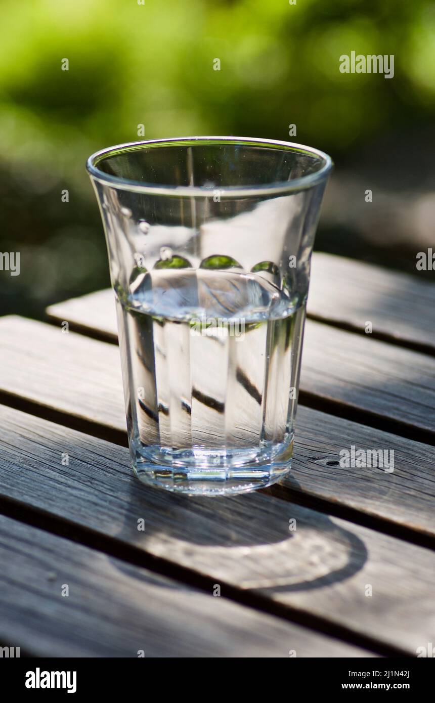 Drinking glass with fresh still water on a wooden table outdoors in summer. Stock Photo