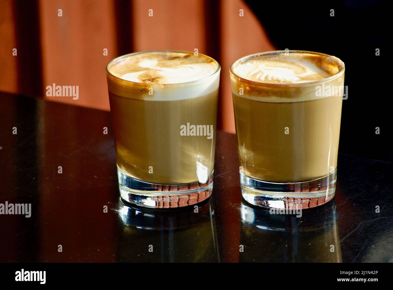 Two glasses of cappuccino in front of a red wooden house wall outdoors in autumn. Stock Photo