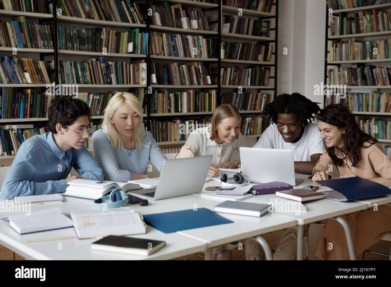 Group of multiethnic students studying together in library using laptop ...