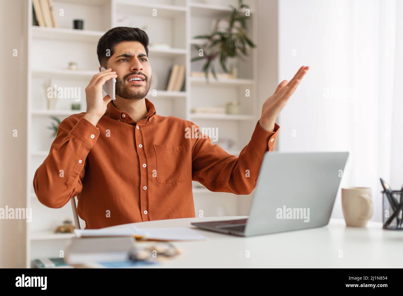 Angry Arab man talking on cell phone using laptop Stock Photo