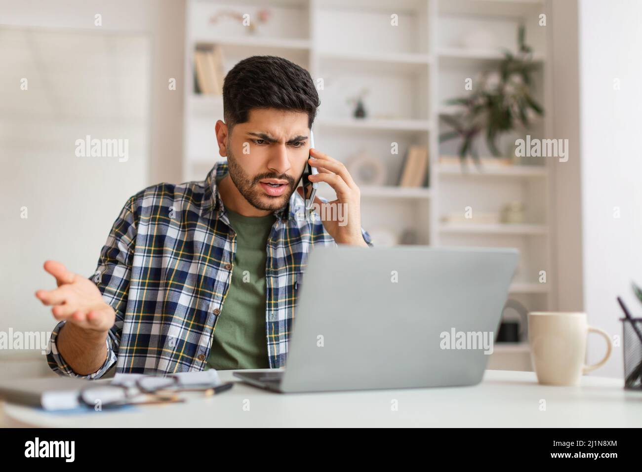Angry Arab man talking on cell phone using laptop Stock Photo