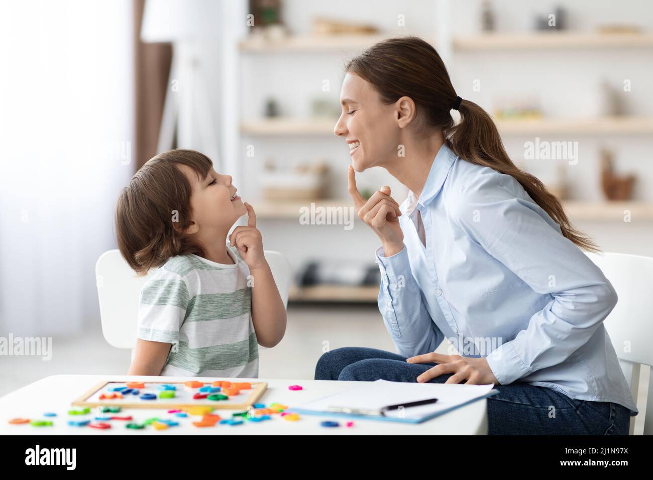 Speech training for kids. Professional woman training with little boy at cabinet, teaching right articulation exercises Stock Photo