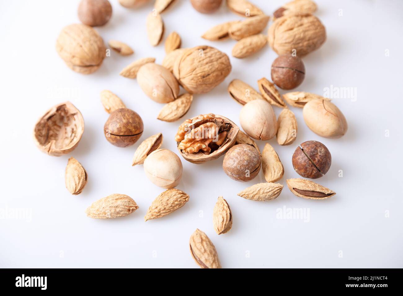 Assorted nuts in the shell on a white background: walnuts, pecans, almonds, macadamia. Selective focus, close-up. Stock Photo