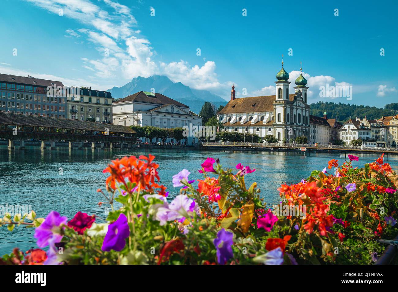 Famous touristic and travel destination in Lucerne. Jesuitenkirche church and Reuss river. Waterfront view with flowered wooden Chapel bridge, Luzern, Stock Photo