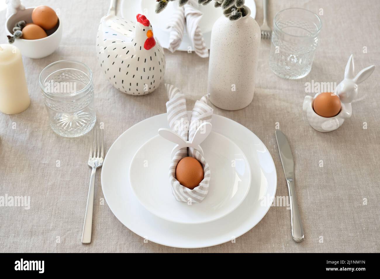 Easter table setting with egg in Easter bunny napkin on plate. Easter table serving. Stock Photo