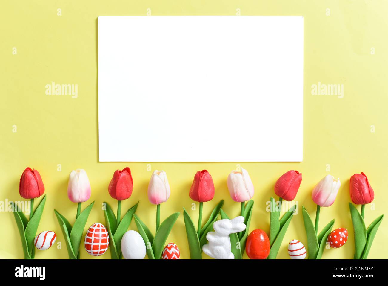 Background with tulips and Easter eggs on a yellow background with a white sheet of paper. Stock Photo
