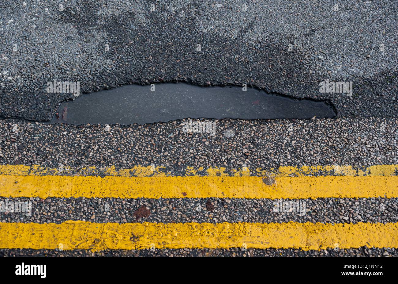 Pothole filled with rainwater by double yellow lines in a UK town centre Stock Photo