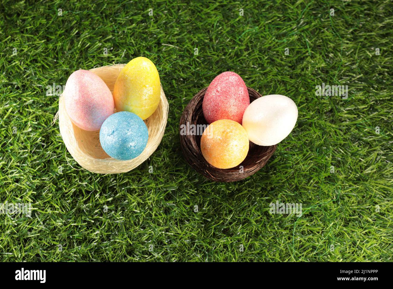 Two Easter Egg nests each with three colourful, sparkly eggs inside against a grass background. Stock Photo