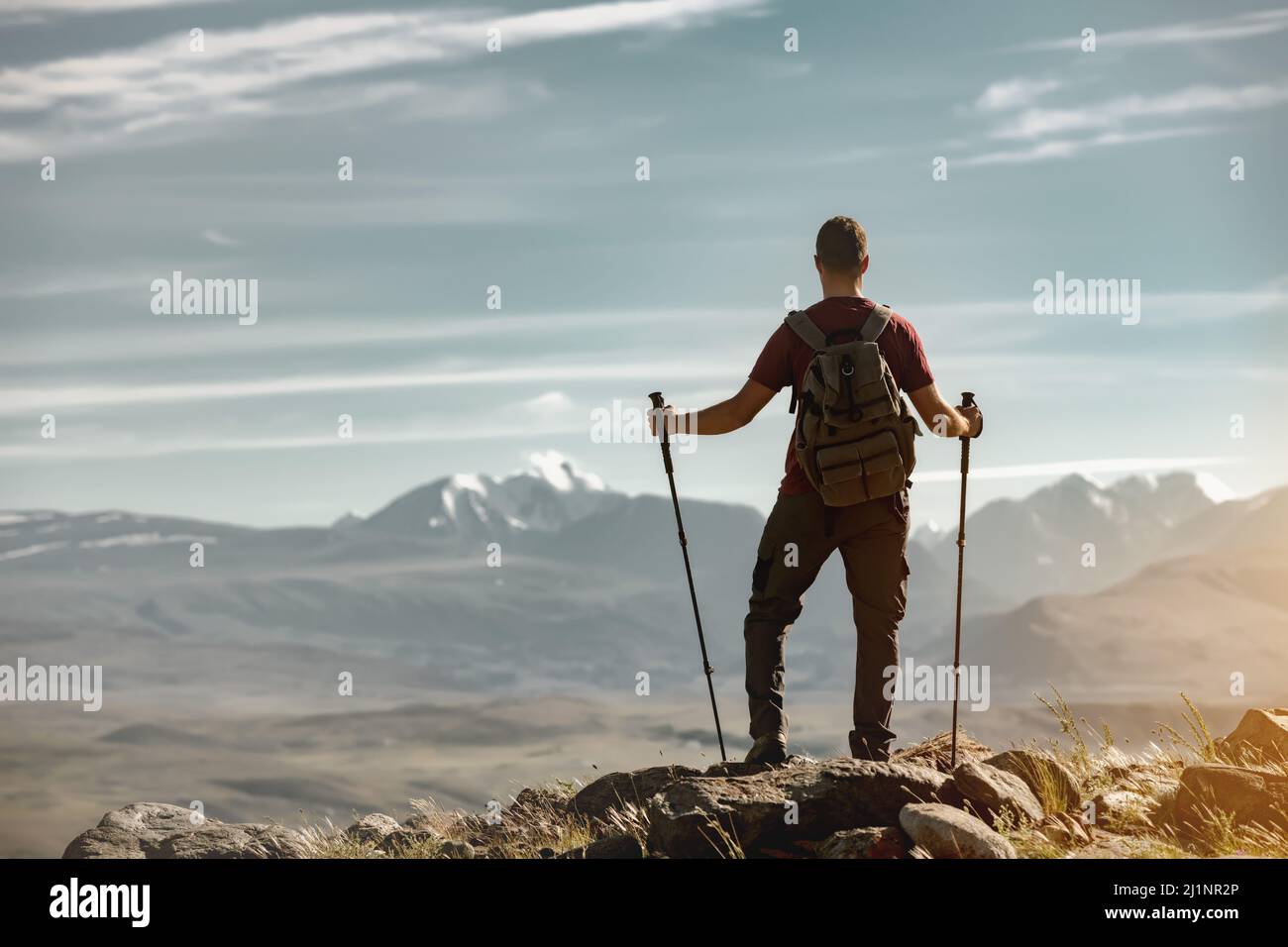 Tourist with backpack and hiking poles stands in mountains and looks at the view Stock Photo