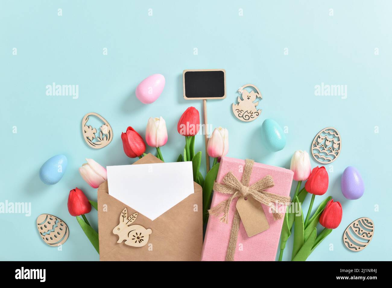 A bouquet of tulips with a postcard, a gift and wooden Easter eggs with ...