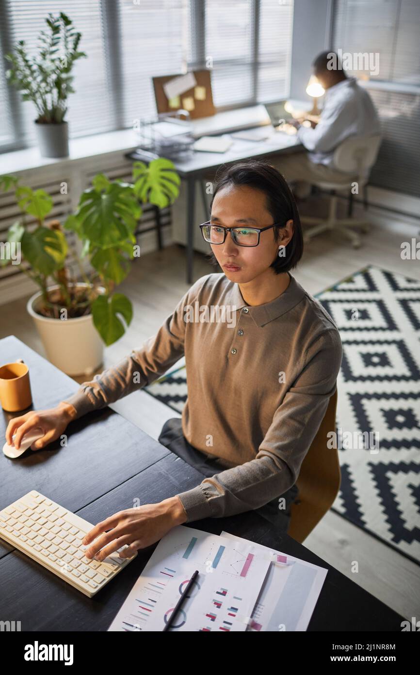 Vertical portrait of Asian software developer using computer while working late at office Stock Photo