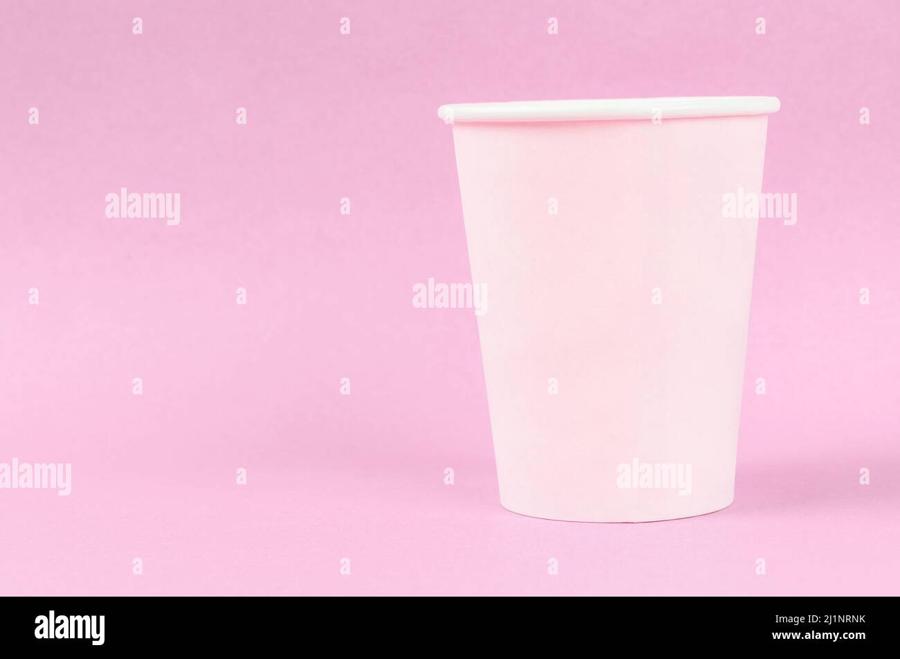 Pink disposable paper cups on pink background with empty space. Stock Photo