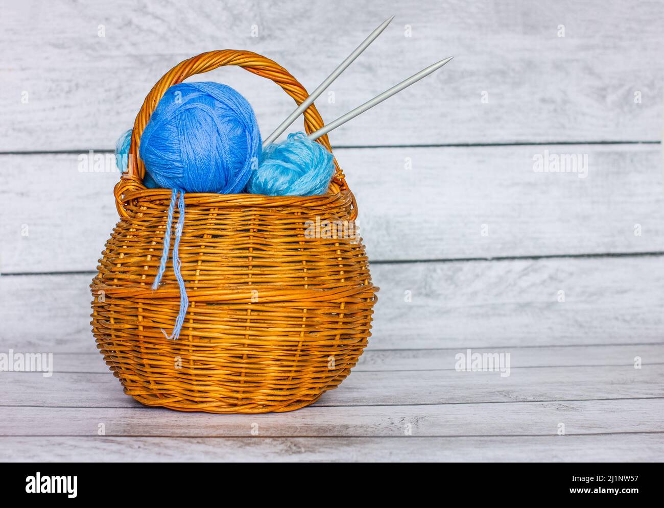 A set of blue woolen threads of different sizes, knitting needles, inside a wicker basket. Home hobby. Knitting. Balls of yarn. Stock Photo