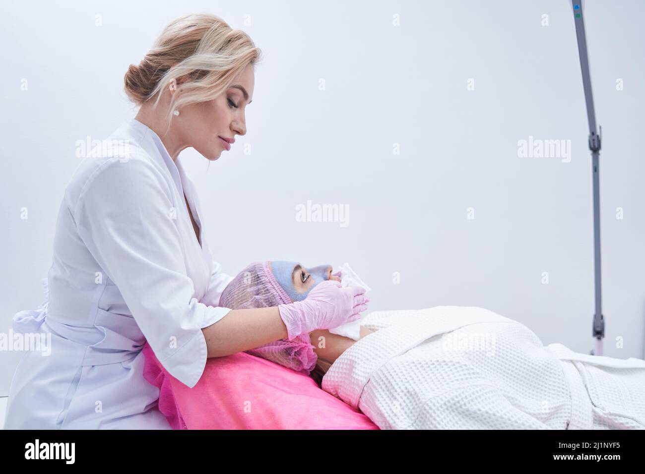 Concentrated dermatologist wetting female face with damp facecloths