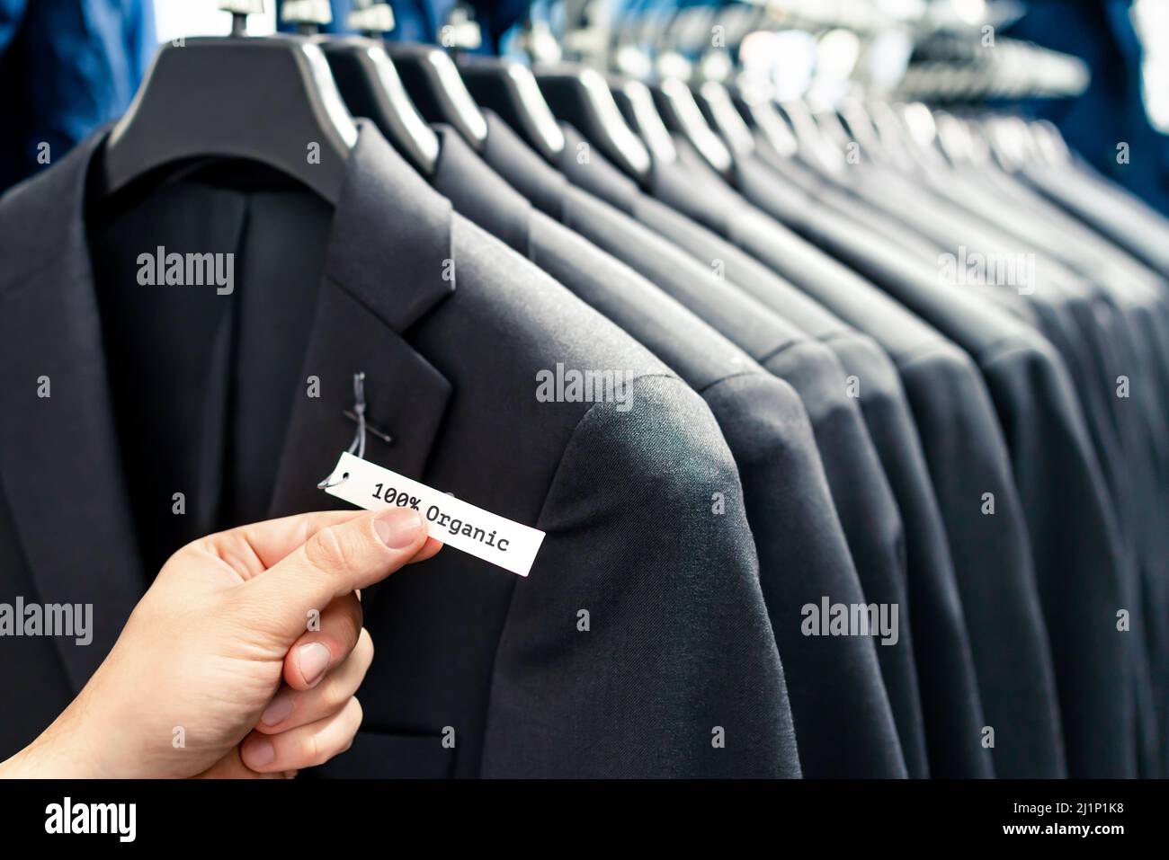 Organic suit jackets with label tag. Ethical men fashion. Customer in sustainable retail store. Quality product made from natural fabric and textile. Stock Photo