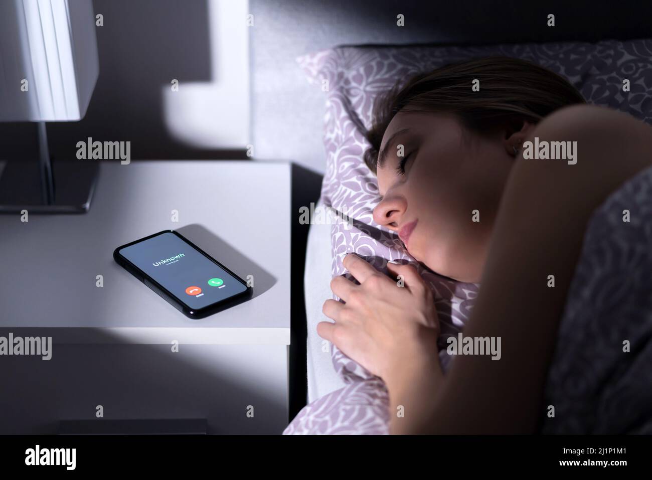 Phone call by unknown caller at night while woman is sleeping in bed. Scam, fraud or mobile hoax from suspicious fake number. Illegal mobile crime. Stock Photo