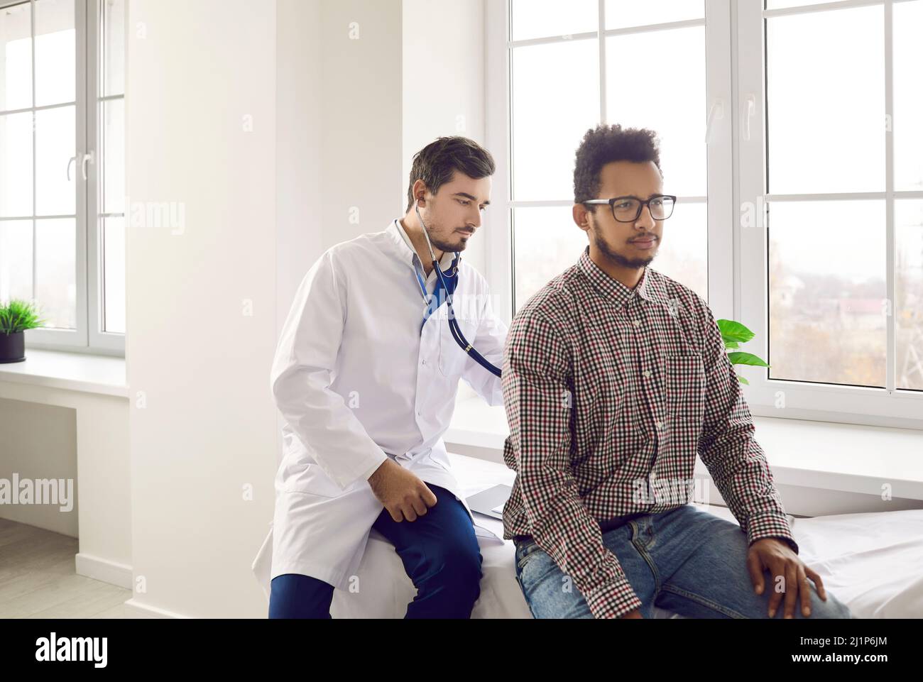 Doctor using stethoscope to check respiration or heartbeat of young male patient Stock Photo