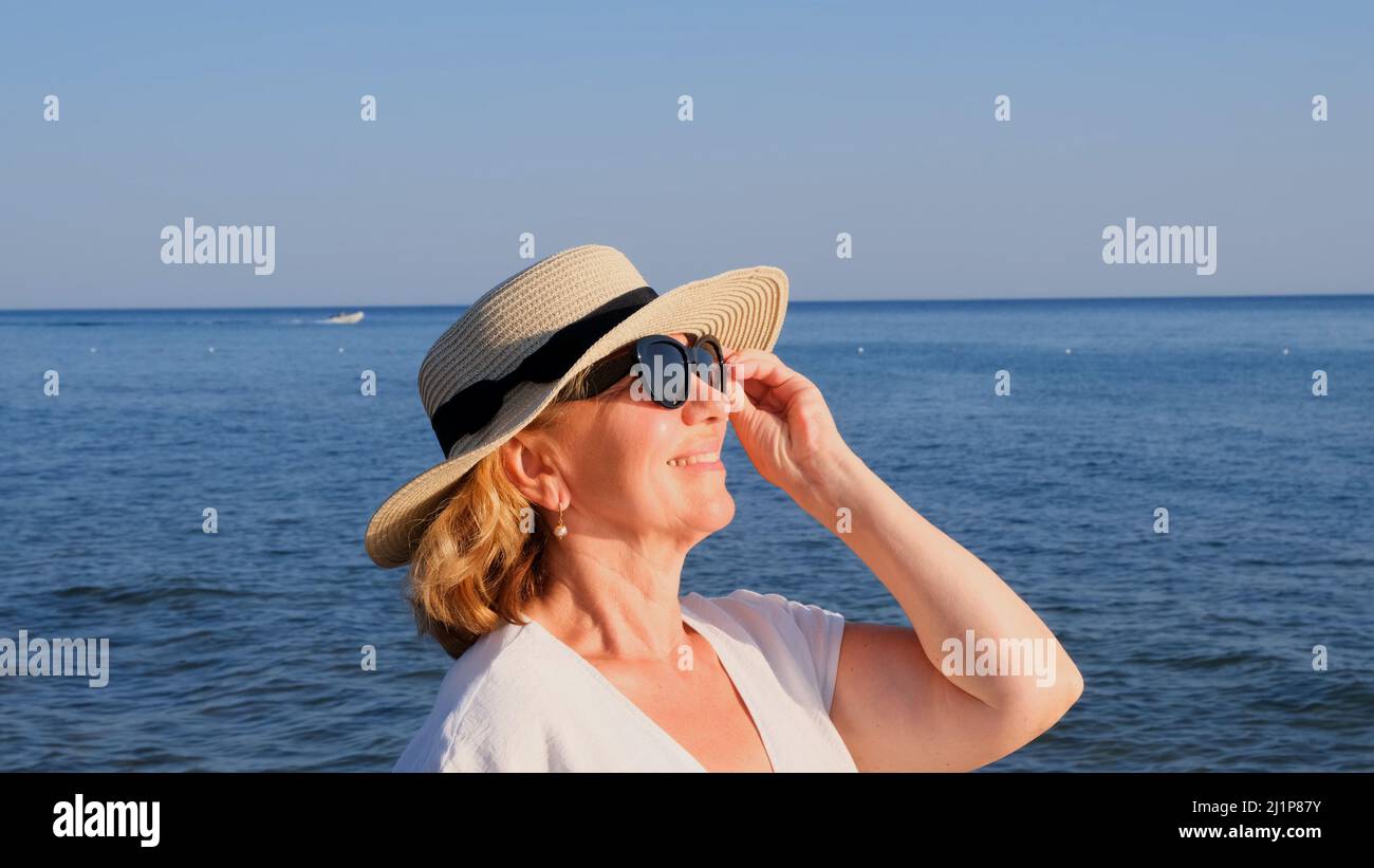 beautiful 50 year old woman in a straw hat and sunglasses on a blue sea